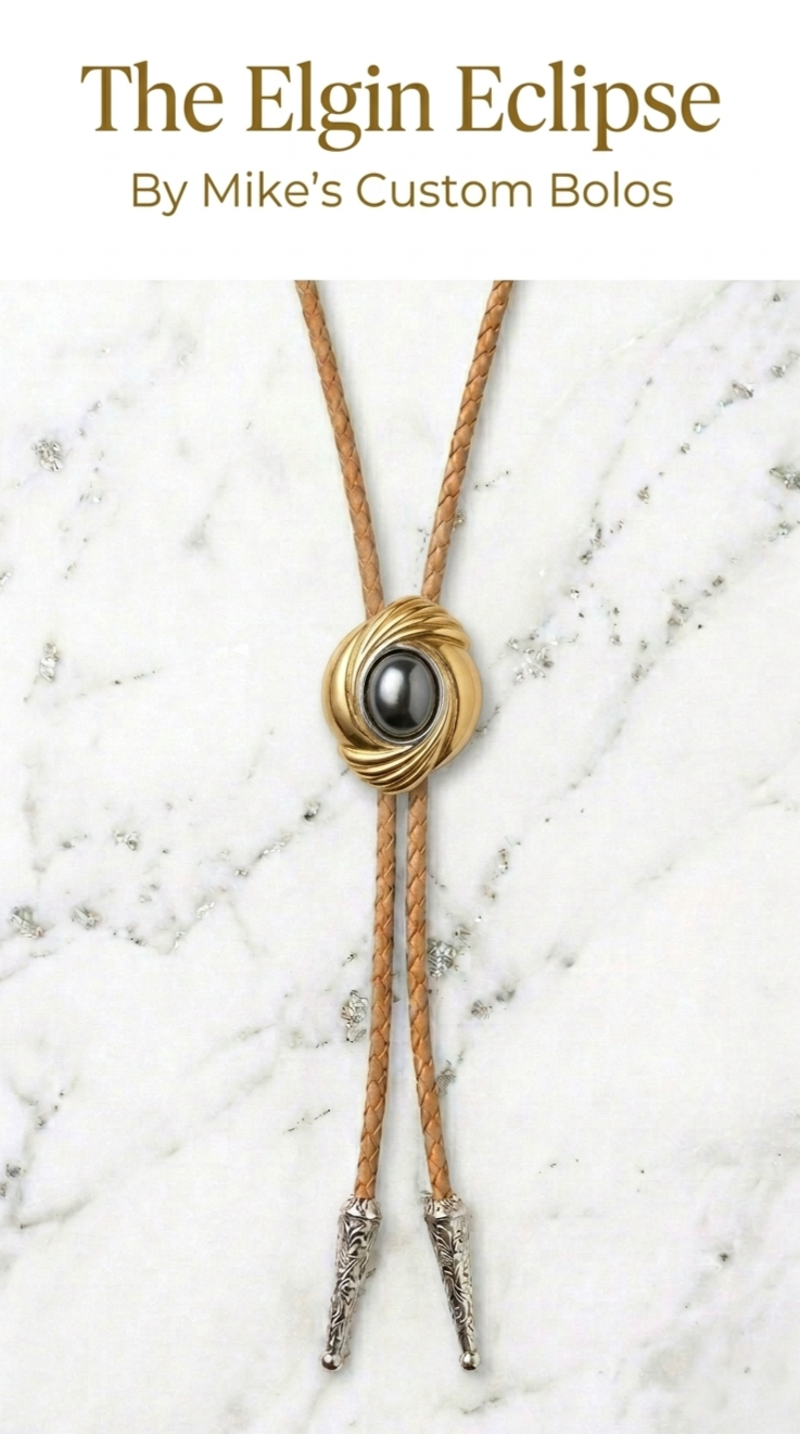 Bolo tie with gold clasp and black stone on a marble background, branded 'The Elgin Eclipse by Mike's Custom Bolos'.