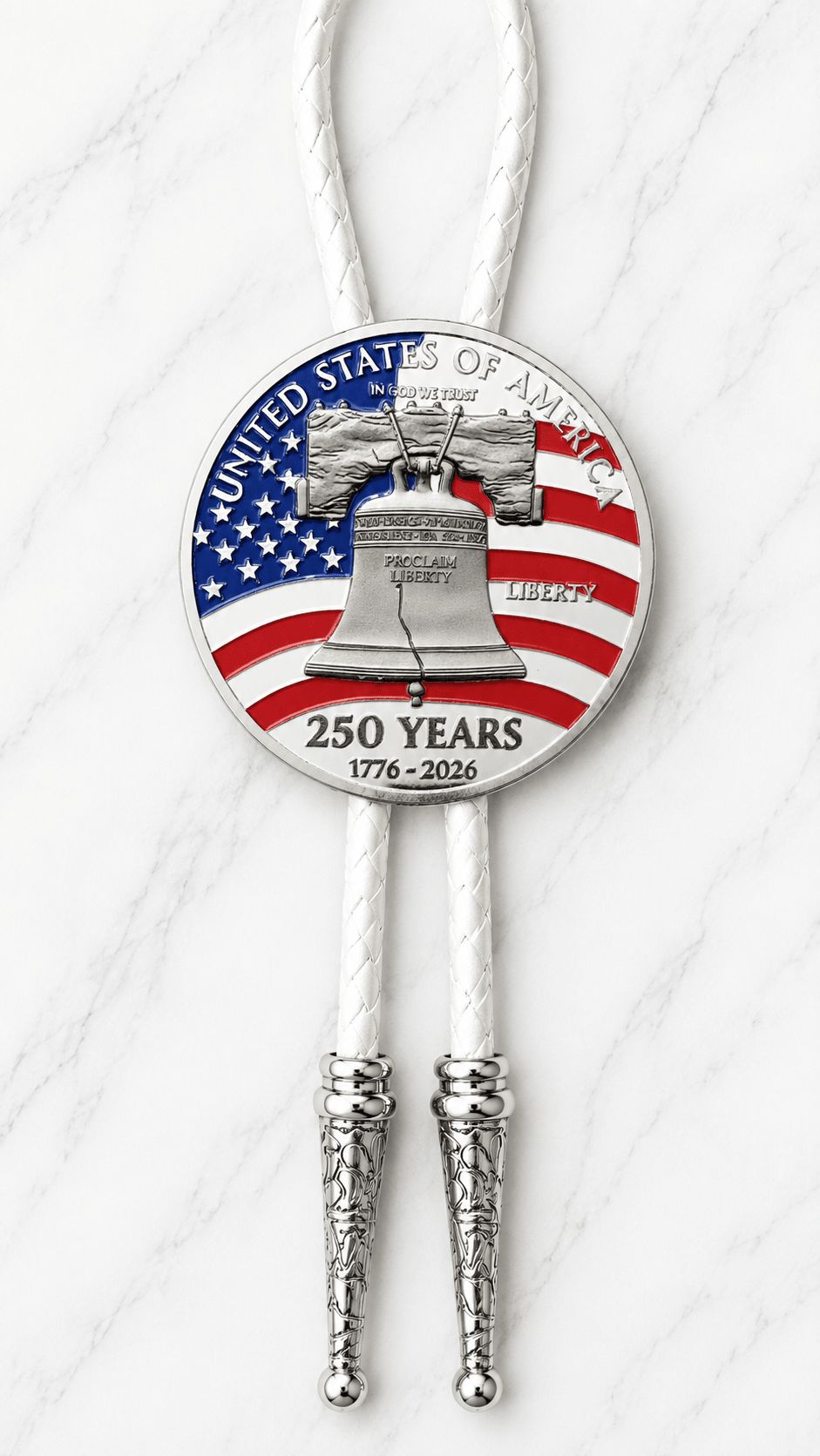 The Liberty Bell Bolo Tie Side A with a Liberty Bell 250 Years commemorative coin, white braided leather, and ornate silver bolo tips displayed on a white marble background