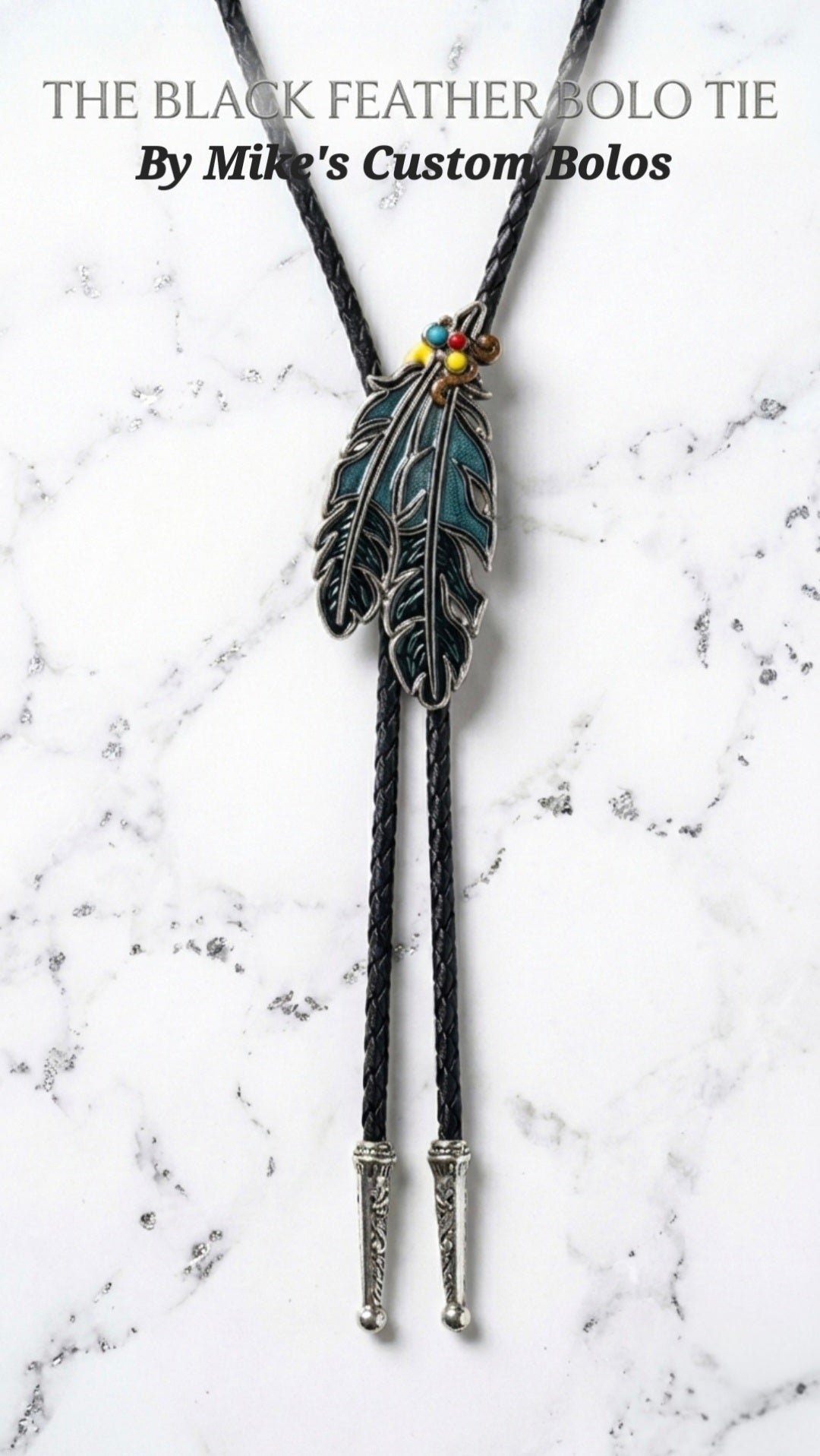The Black Feather Bolo Tie by Mike's Custom Bolos displayed on a white marble background with black braided cord and feather centerpiece.